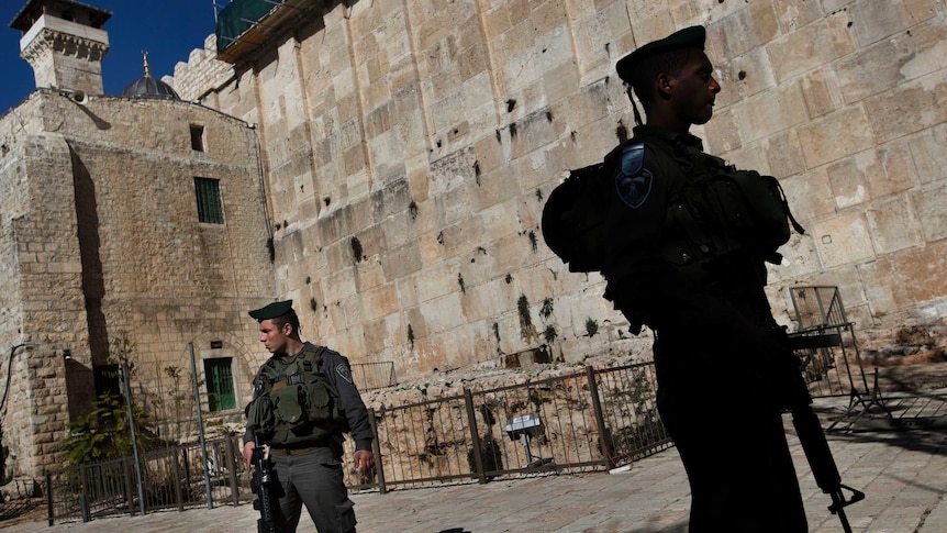 Soldiers with guns stand in front of a high wall in Hebron.