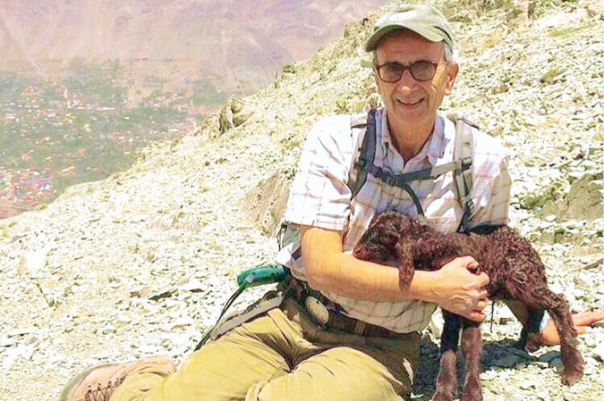 Professor Kavous Seyed-Emami seated on a mountainside, holding a small goat and wearing hiking gear