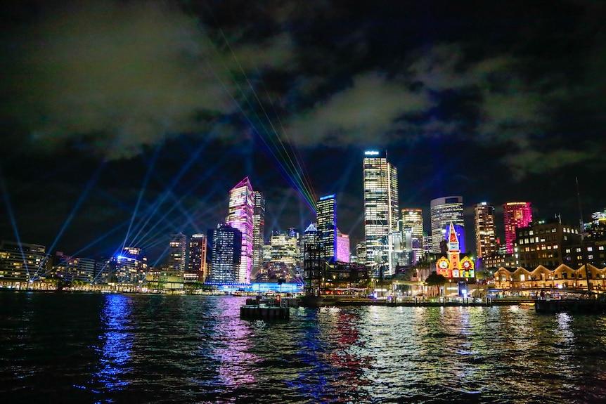 Looking back over the harbour the city of Sydney is lit up with a number of colourful lights.