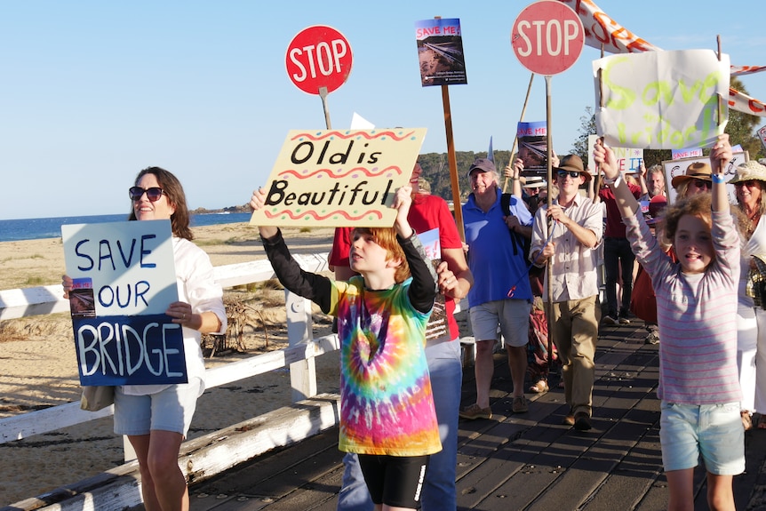 Protestors with signs on a wooden bridge.