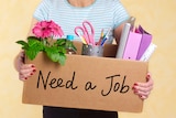 A woman holding cardboard box which says 'need a job' on the side.