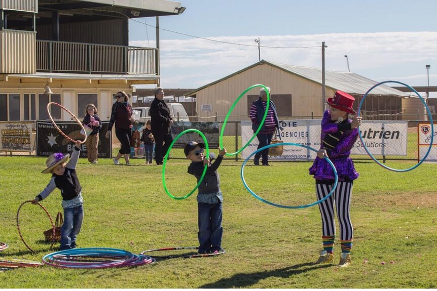 Woman dressed is top hat, marching band blazer and striped black and white pants perfoms act with Hula Hoops for children