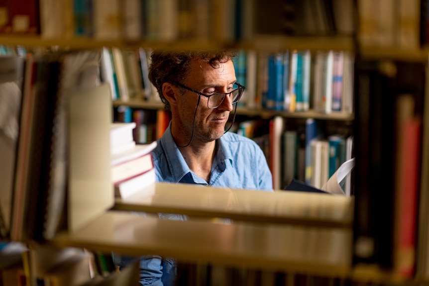 The face of Dr Charlie Ward is seen through a the bookshelf at the NT Library.