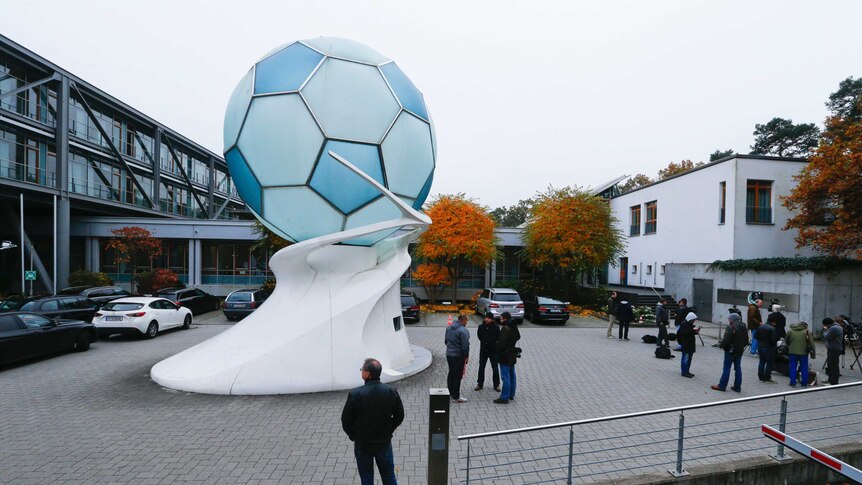 People mill around a car park next to a large soccer ball sculpture