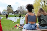 Two young women with their back to the camera look at rows of gravestones 