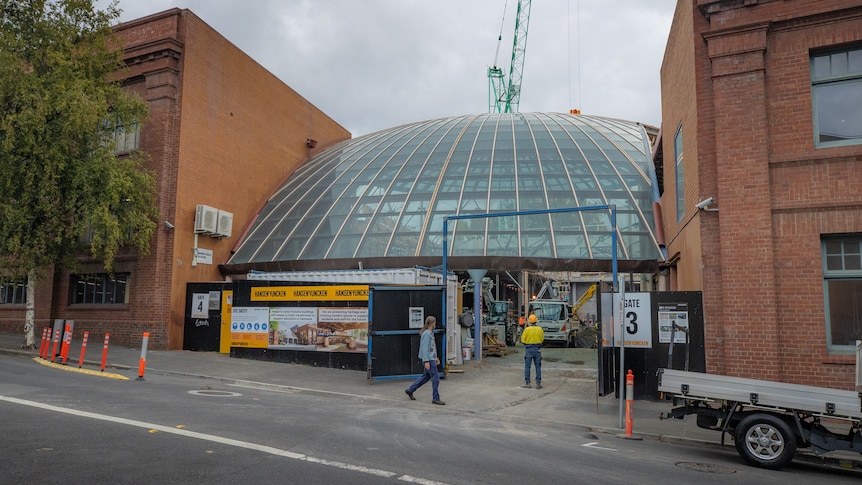 A glass domed building in between two other buildings with construction crew on site.