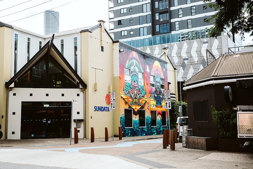 A picture looking down Fish Lane, in Brisbane, showing a colourful mural on the side of a cream coloured building.