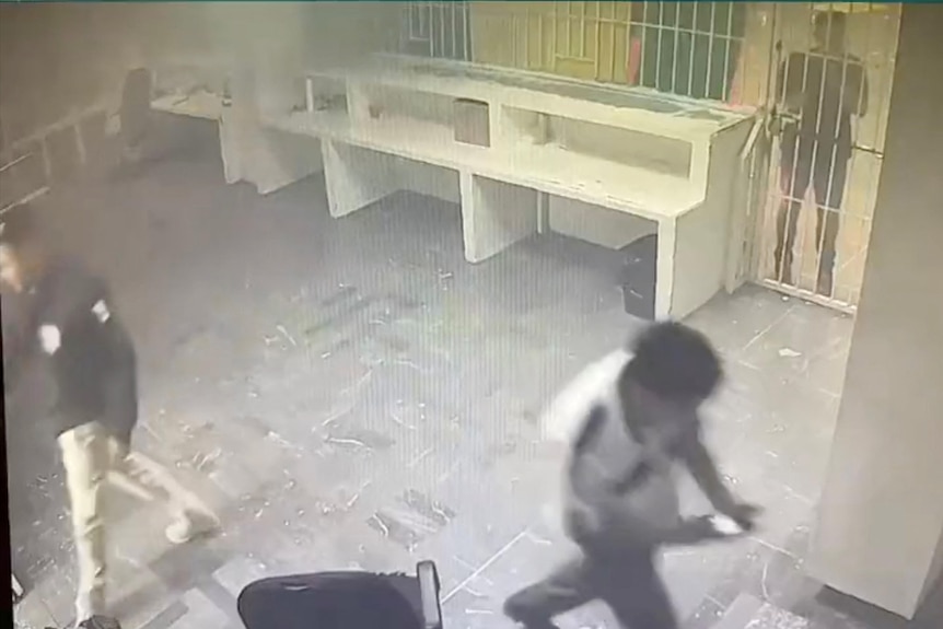 CCTV shows person walking while another person stands behind bars in what appears to be a smoky room.