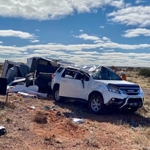 White 4WD towing a caravan crushed following an accident. Other emergency vehicles on the scene.