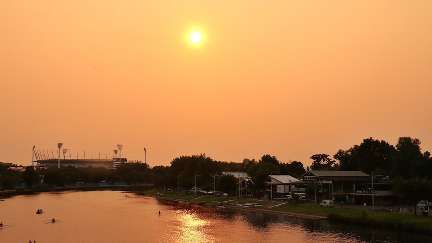 An orange-tinged view of the sun over the Yarra River taken from Princes Bridge facing East.
