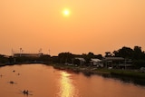 An orange-tinged view of the sun over the Yarra River taken from Princes Bridge facing East.