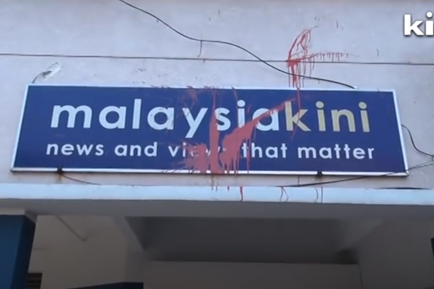 A sign reading 'Malaysiakini news and views that matter' is splattered with red paint.
