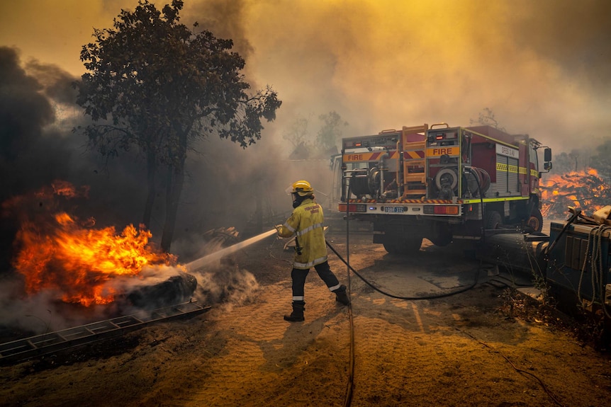 A DFES firefighter tackles flames with a hose at King Road during the Oakford Bushfire