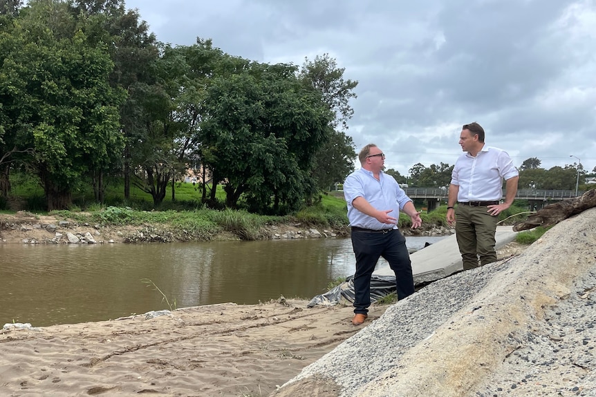 Two men stand beside a damaged creek