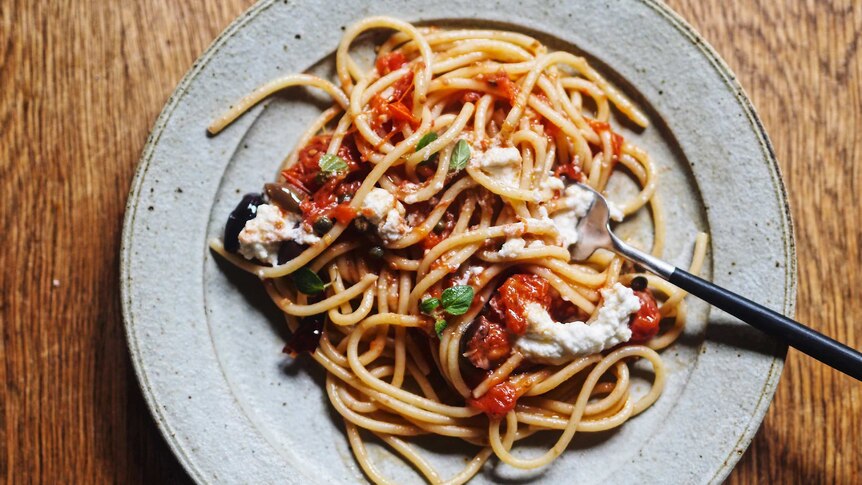 A plate of spaghetti alla Puttanesca with olives, tinned tomato and topped with ricotta and oregano, a vegetarian pasta recipe.