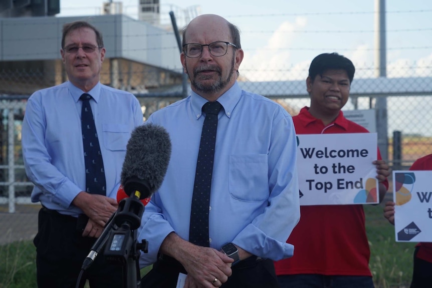 CDU vice chancellor Simon Maddocks addresses the media at Darwin Airport flanked by two other men.