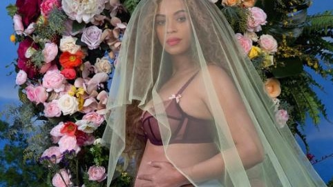 Beyonce caresses her pregnant belly while wearing a veil in front of a floral arrangement