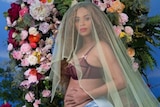 Beyonce caresses her pregnant belly while wearing a veil in front of a floral arrangement