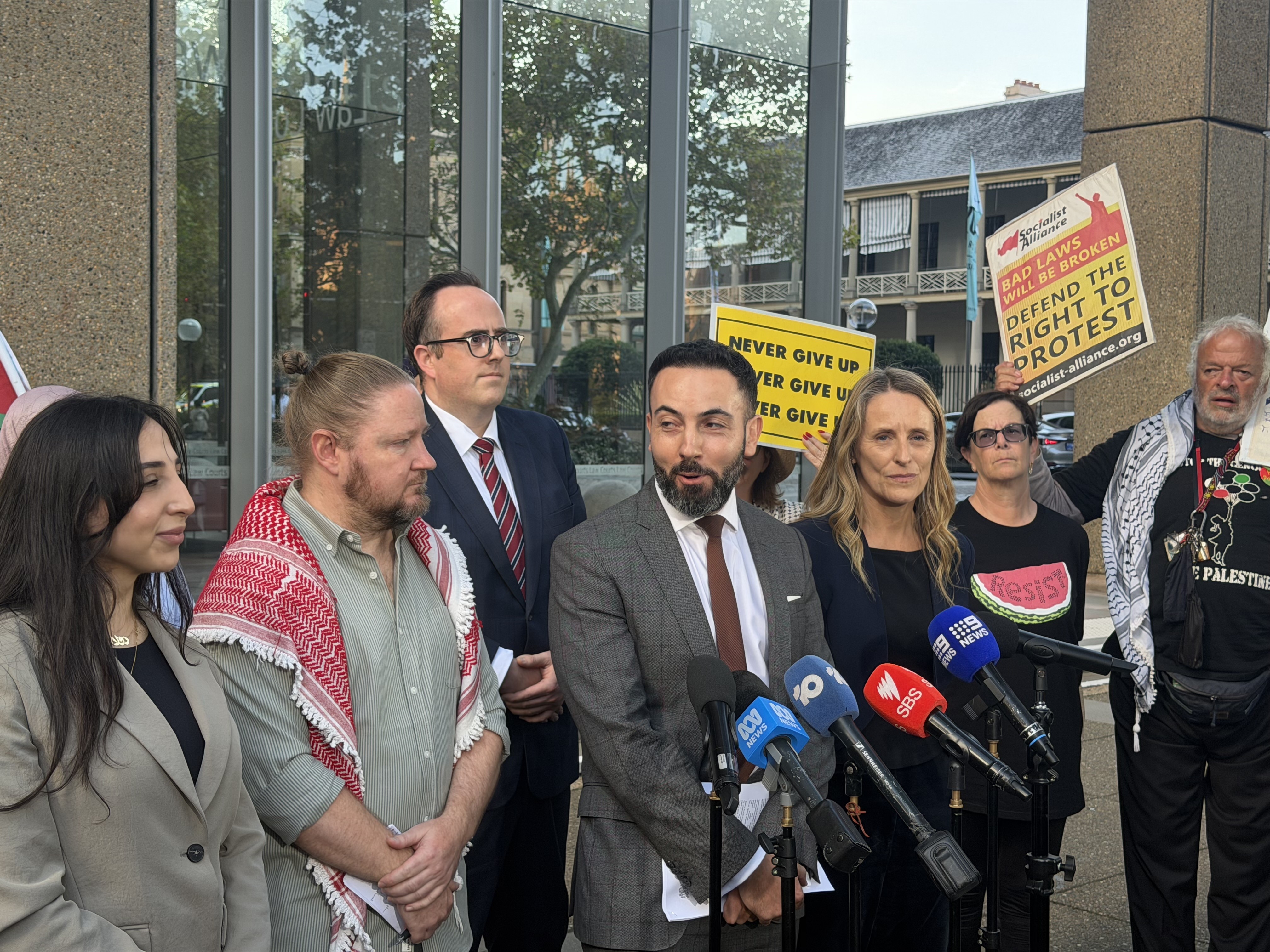A group of people stand behind microphones outside court.