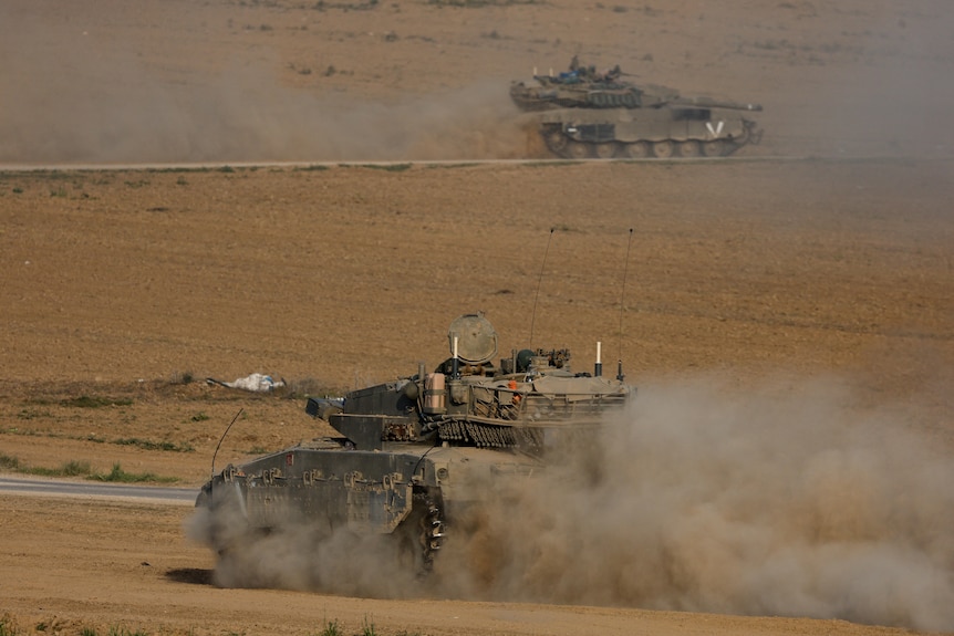 A tank manoeuvres across barren brown ground, leaving a thick trail of dust behind.