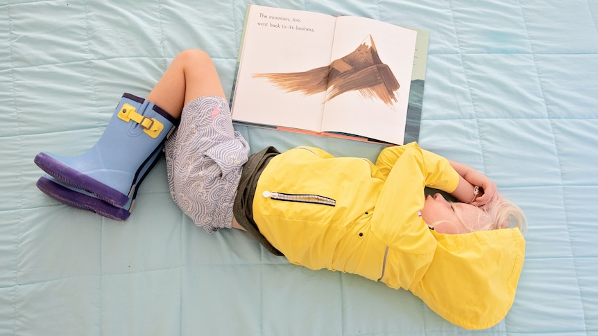 Child sleeping on a bed with an open book by his side. 