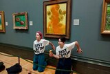 Two people kneel below a Van Gogh painting. 