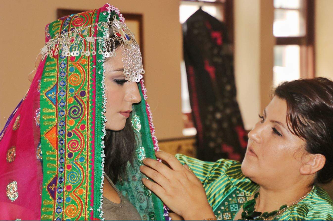 A woman wears a scarf with a silver headdress holding it in place. The designer makes an adjustment.