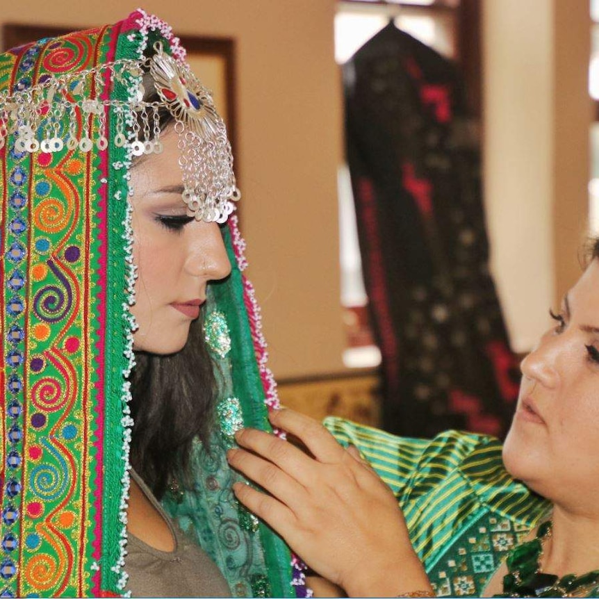 A woman wears a scarf with a silver headdress holding it in place. The designer makes an adjustment.