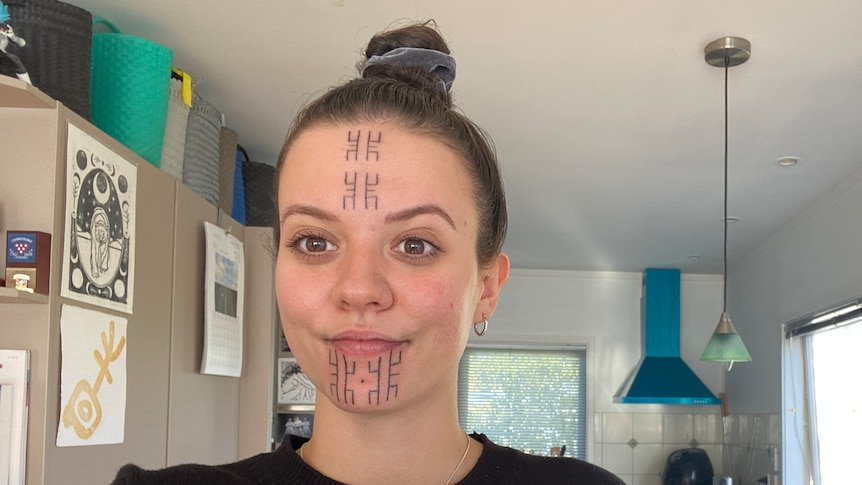 A woman with traditional facial markings takes a selfie