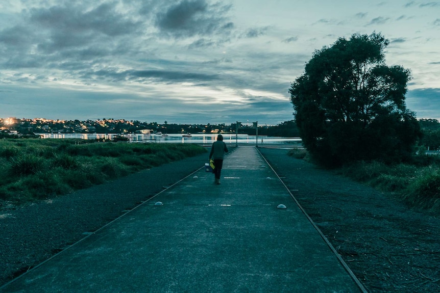 Louis Giles walking to walking towards a bay to work at dusk with an esky in hand.