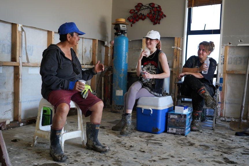 Three women sitting in a house that's been damaged by floods.