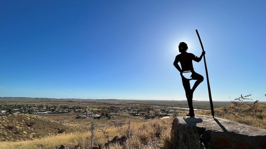 Silhouette of the statue of an Aboriginal hunter holding a spear and looking over the town of Roebourne from the top of a hill