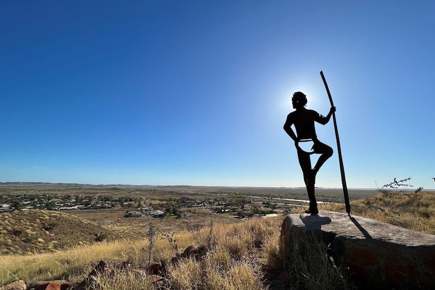Silhouette of the statue of an Aboriginal hunter holding a spear and looking over the town of Roebourne from the top of a hill