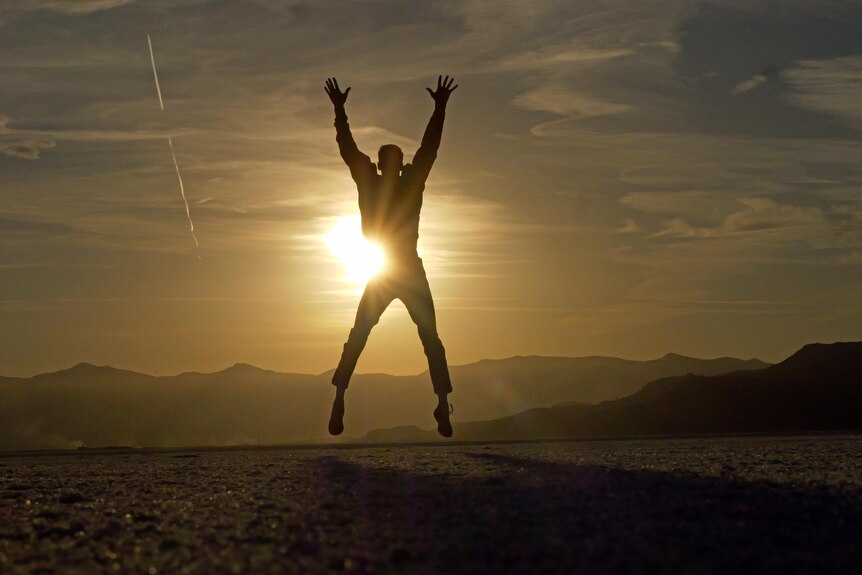 A person doing a star jump in front of a sunrise and mountains