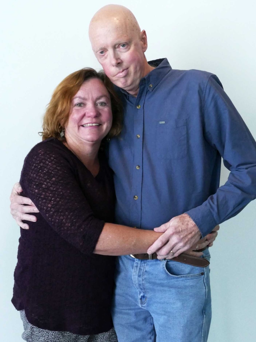 A man and woman stand together hugging.