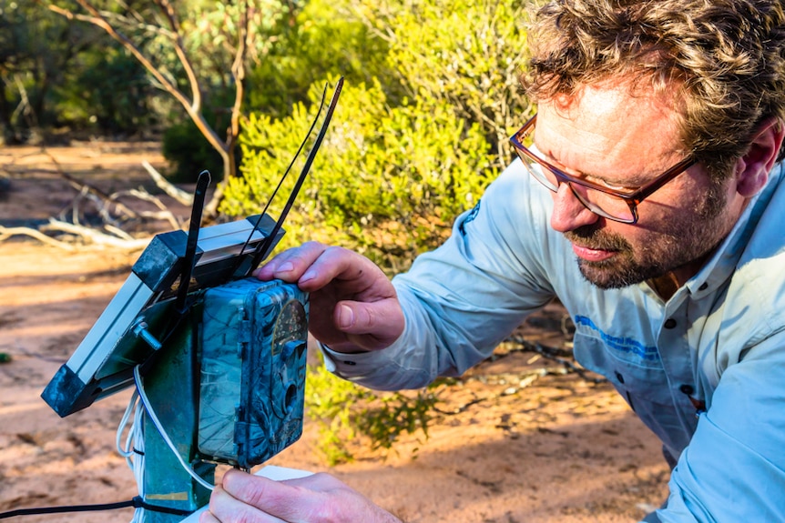 A man has his hands on a small box which is connected to a camera. He is concentrating on the device.