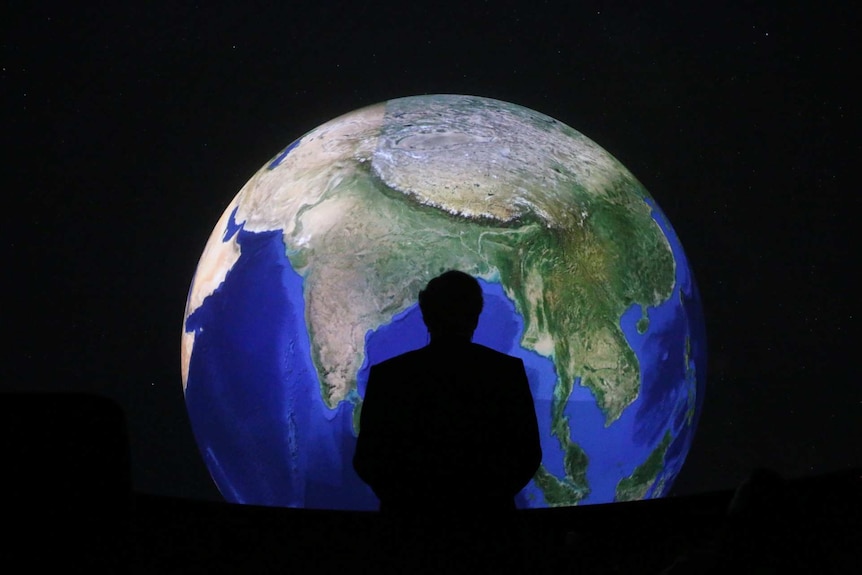 The silhouette of a man standing on from of a globe.