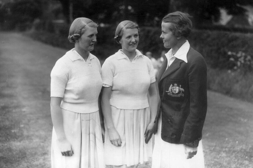Two young women in whites speak to Margaret Peden, who is in her Australian cricket team blazer.
