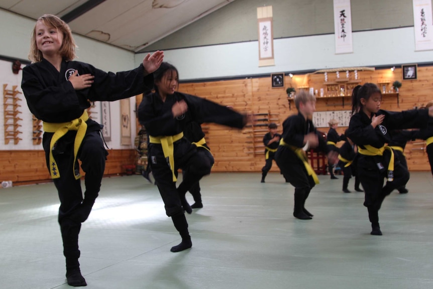 Eight-year-old Emily smiles and balances on one leg while dressed in her ninja uniform during a ninja class in Hobart.