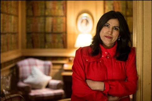 Jasvinder Sanghera standing in a doorway of warmly lit room, arms crossed, smiling a little.