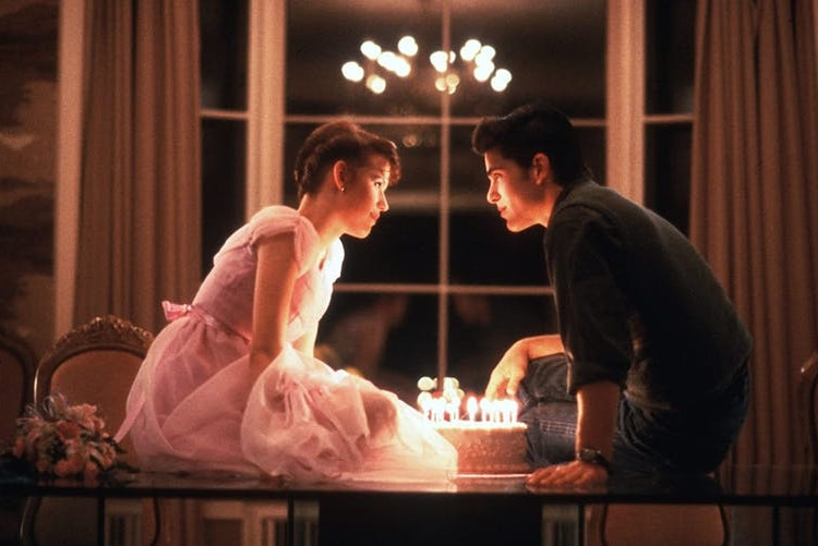 A girl in a pink dress and a boy lean into kiss over a birthday cake