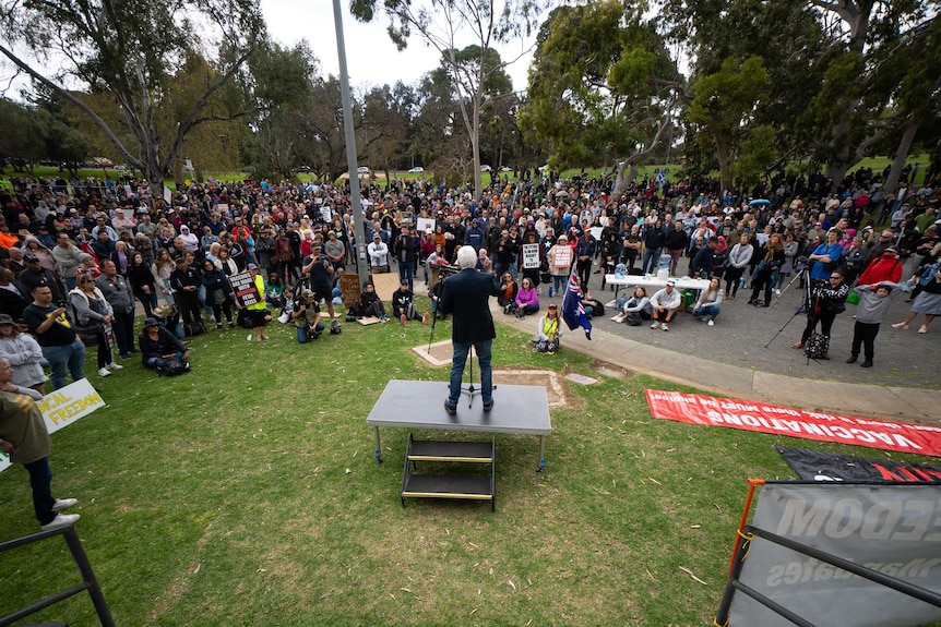 A man speaks to other people gathered in a park with protest signs