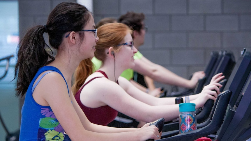 Two woman smile while using exercise bikes in a gym