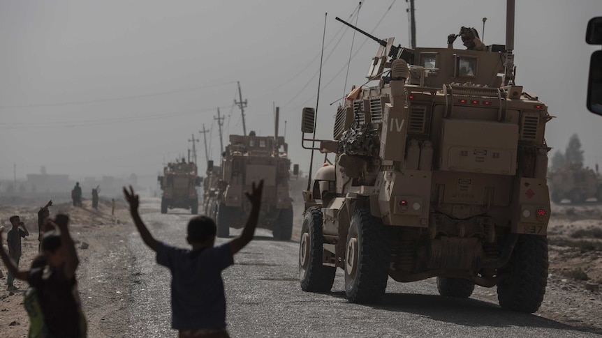 Children watch military vehicles pass by in the village of Imam Gharbi, some 70km south of Mosul, Iraq, on October 13, 2016.