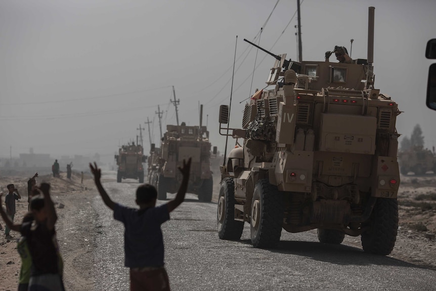 Children watch military vehicles pass by in the village of Imam Gharbi, some 70km south of Mosul, Iraq, on October 13, 2016.