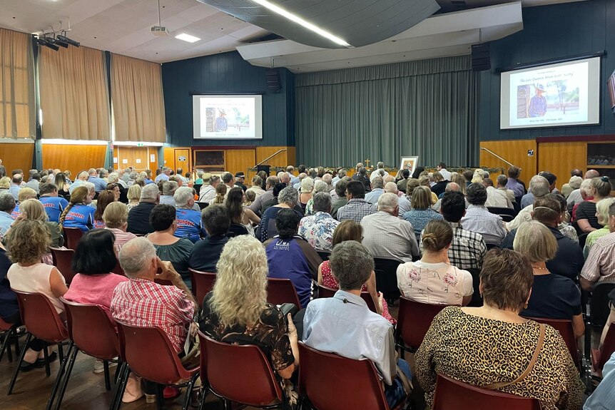 A crowd of people on chairs in a room look towards the front of the stage.