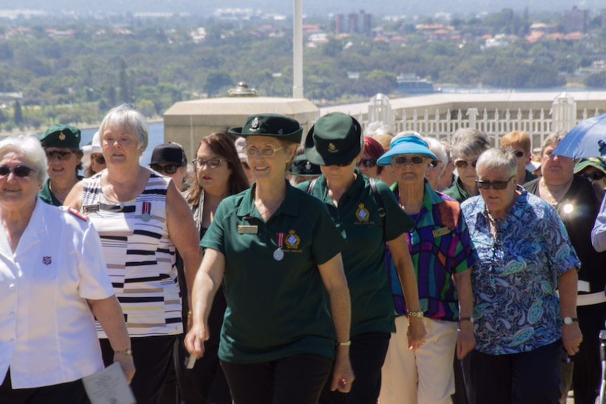 A large group of women, some in uniform and others in casual clothing, as they march in Kings Park with Perth in the background.