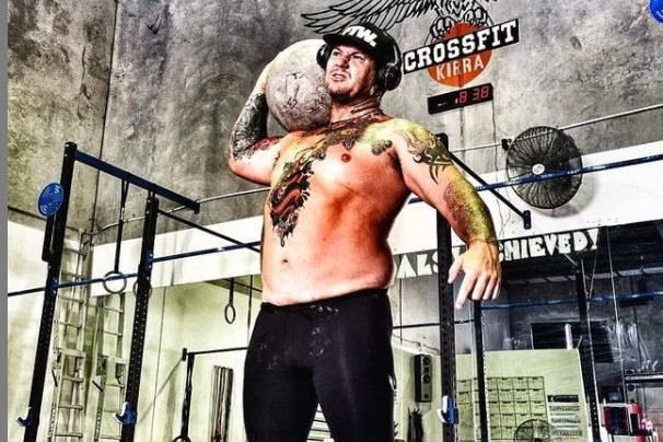 A tattooed man stands in a gym holding a ball.