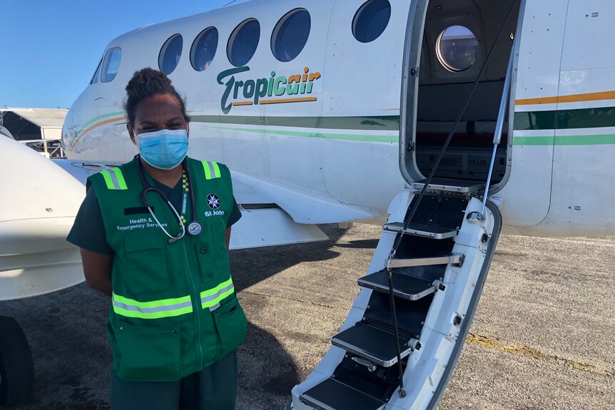 A young Papua New Guinean woman in green paramedic gear stands next to a plane