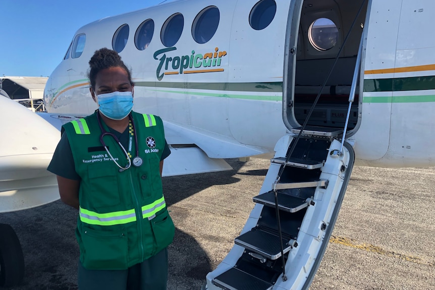 A young Papua New Guinean woman in green paramedic gear stands next to a plane